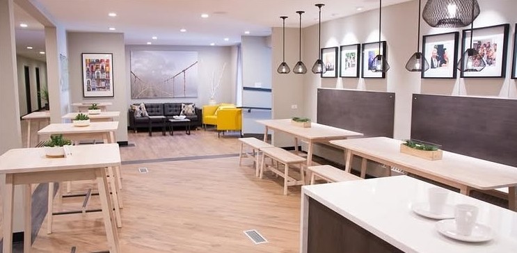 Open dining hall with pale wood tables, pendant lights and framed photos