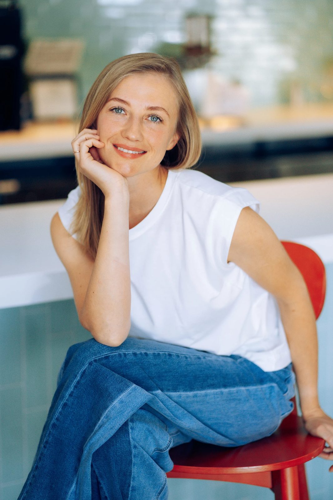 Woman in a white tee and jeans on a red chair in a bright cafe